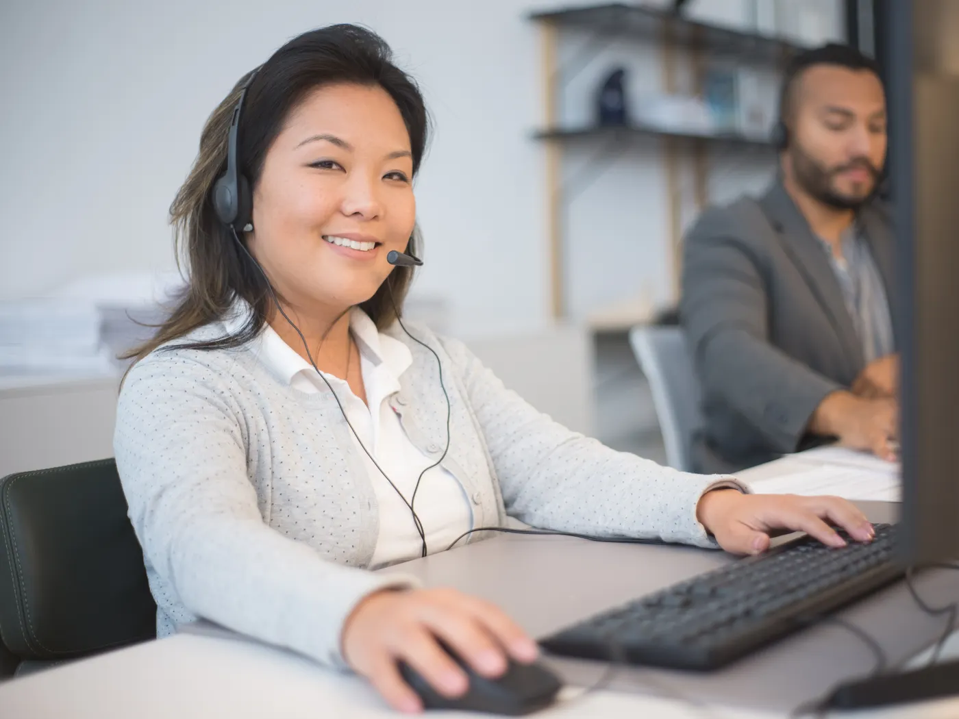 Two colleagues wearing headsets working side by side at their computers